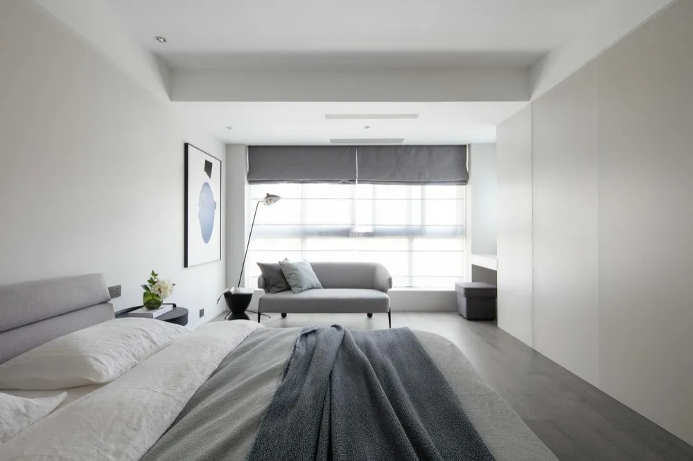 Chambre grise moderne Chambre moderne minimaliste avec lit double, plaid gris, canapé clair près d’une grande fenêtre et décoration épurée, style contemporain lumineux.
