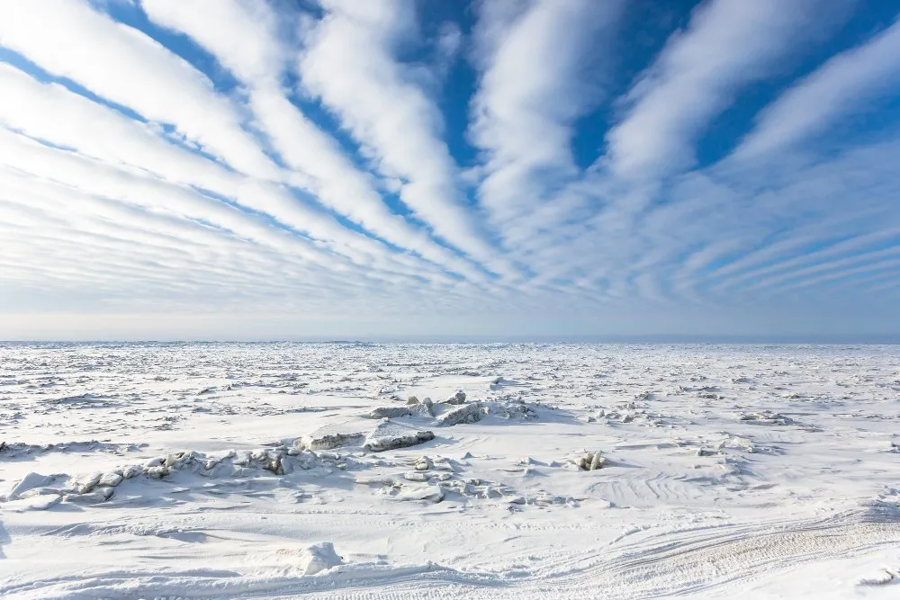 Paysage artique Paysage arctique couvert de glace et de neige, avec un ciel bleu traversé par des nuages en bandes parallèles, formant un effet de perspective spectaculaire.