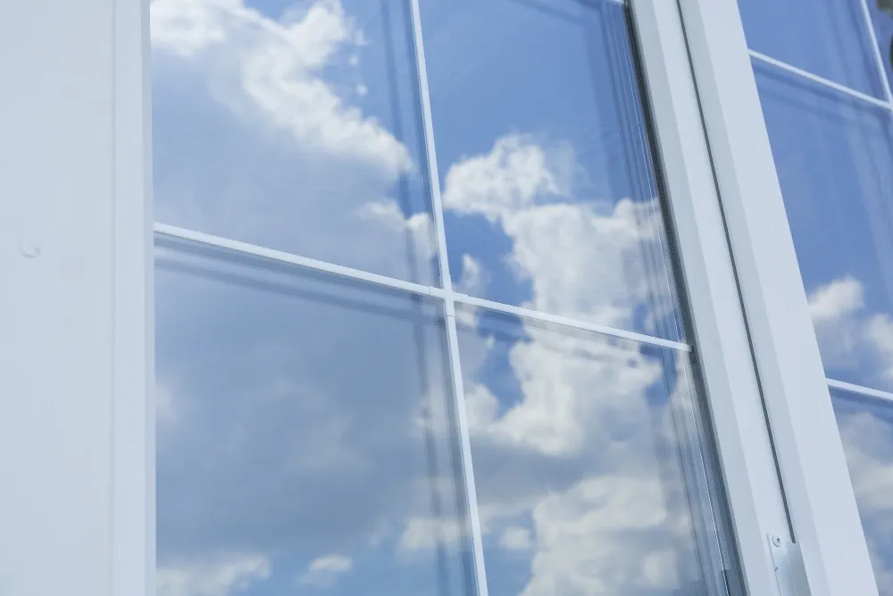 Fenêtres blanches Fenêtre en PVC blanche avec croisillons, reflétant un ciel bleu parsemé de nuages.