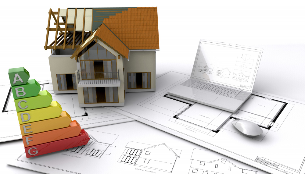 Maquette de maison en construction avec plans d’architecte, ordinateur portable affichant des dessins techniques et échelle de performance énergétique de A à G.